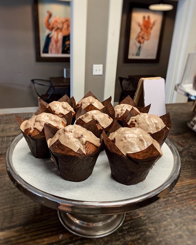 A display of eight chocolate muffins with light-colored frosting on a silver pedestal stand in a cafe.