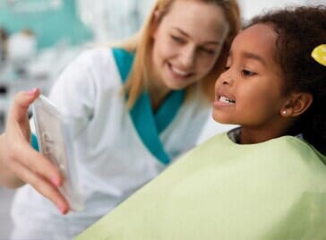 A girl patient showing in mirror her teeth - Dental Services in Sioux City, IA