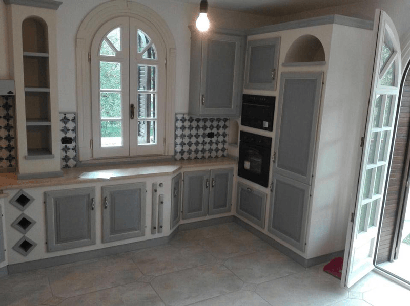 Cucina luminosa con mobili bianchi, finestre ad arco, paraschizzi piastrellato e porte a vetri aperte.