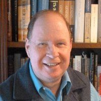 A man is smiling in front of a bookshelf filled with books.