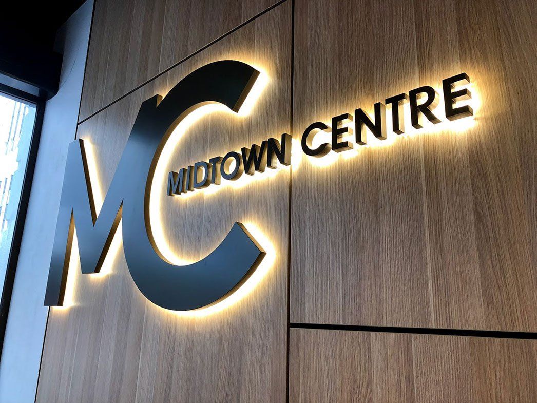 Black Logo With Yellow Backlight On Wood Wall — Signage In Acacia Ridge, QLD