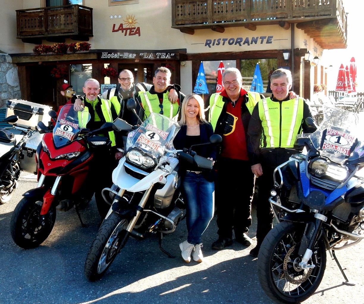 Un gruppo di motociclisti posa con le loro moto fuori da un ristorante. Alcuni indossano giubbotti catarifrangenti.