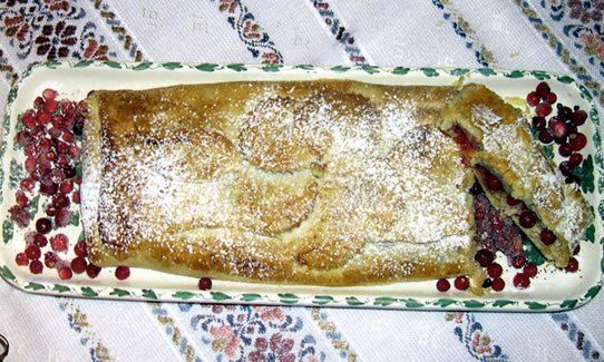 Strudel di mele spolverato con zucchero a velo su un piatto rettangolare con mirtilli rossi.