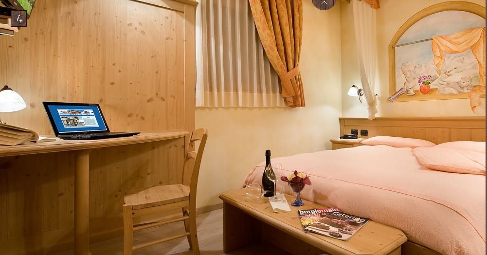 Accogliente camera d'albergo con scrivania in legno, computer portatile e letto con panca, bottiglia di vino.