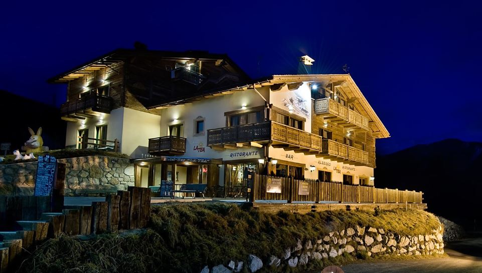 Edificio in stile chalet di notte con luci calde, balconi in legno e base in pietra.