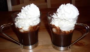 Due bicchieri di cioccolata calda con panna montata, su un tavolo di legno.