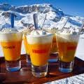 Cinque cocktail all'arancia con panna montata, sullo sfondo montagne innevate.