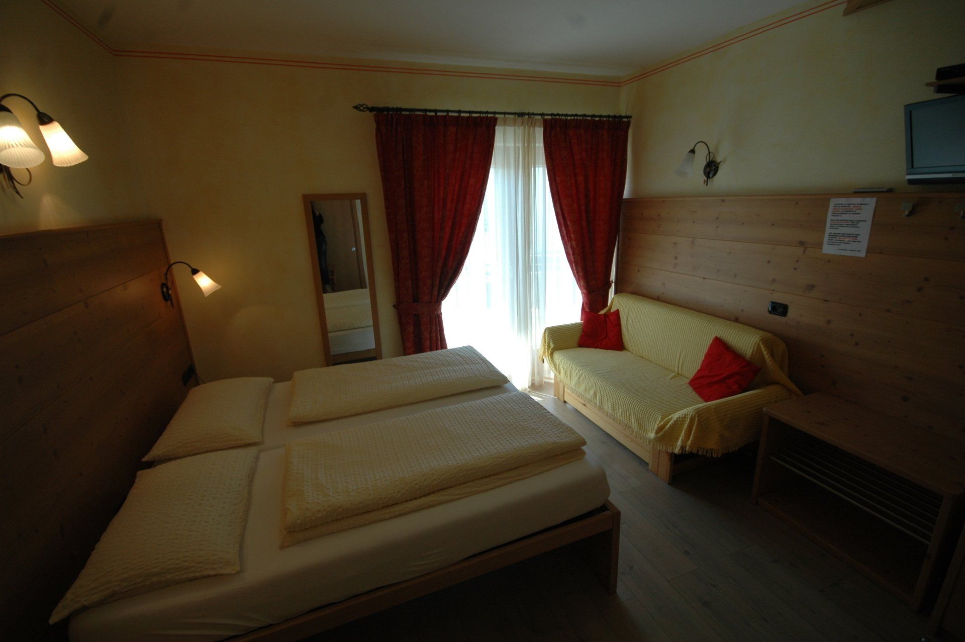 Camera da letto con letto matrimoniale, divano e tende rosse. Pareti beige e mobili in legno.