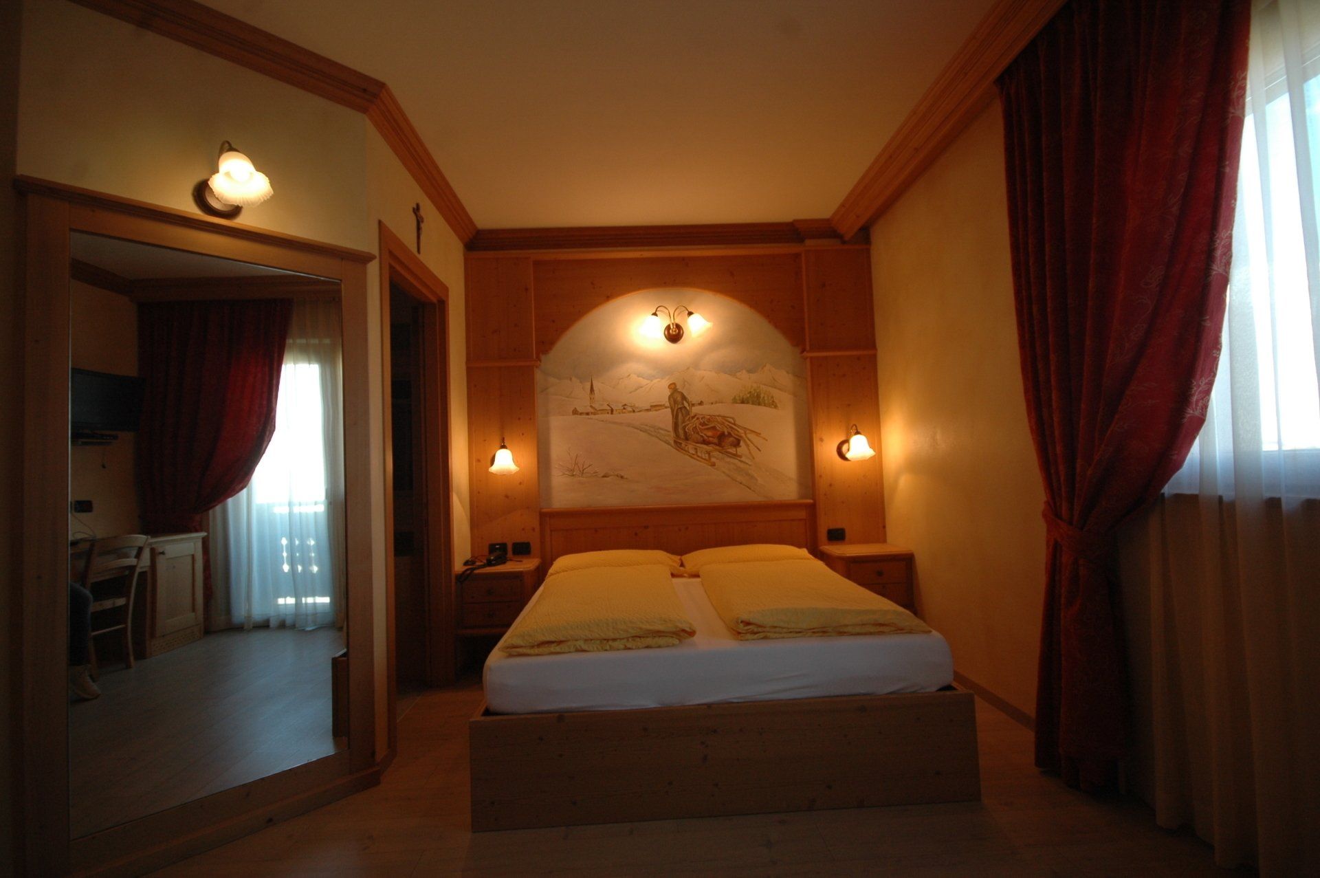 Camera d'albergo con letto, opere d'arte e una porta che conduce a un balcone. Luci calde e tende rosse.