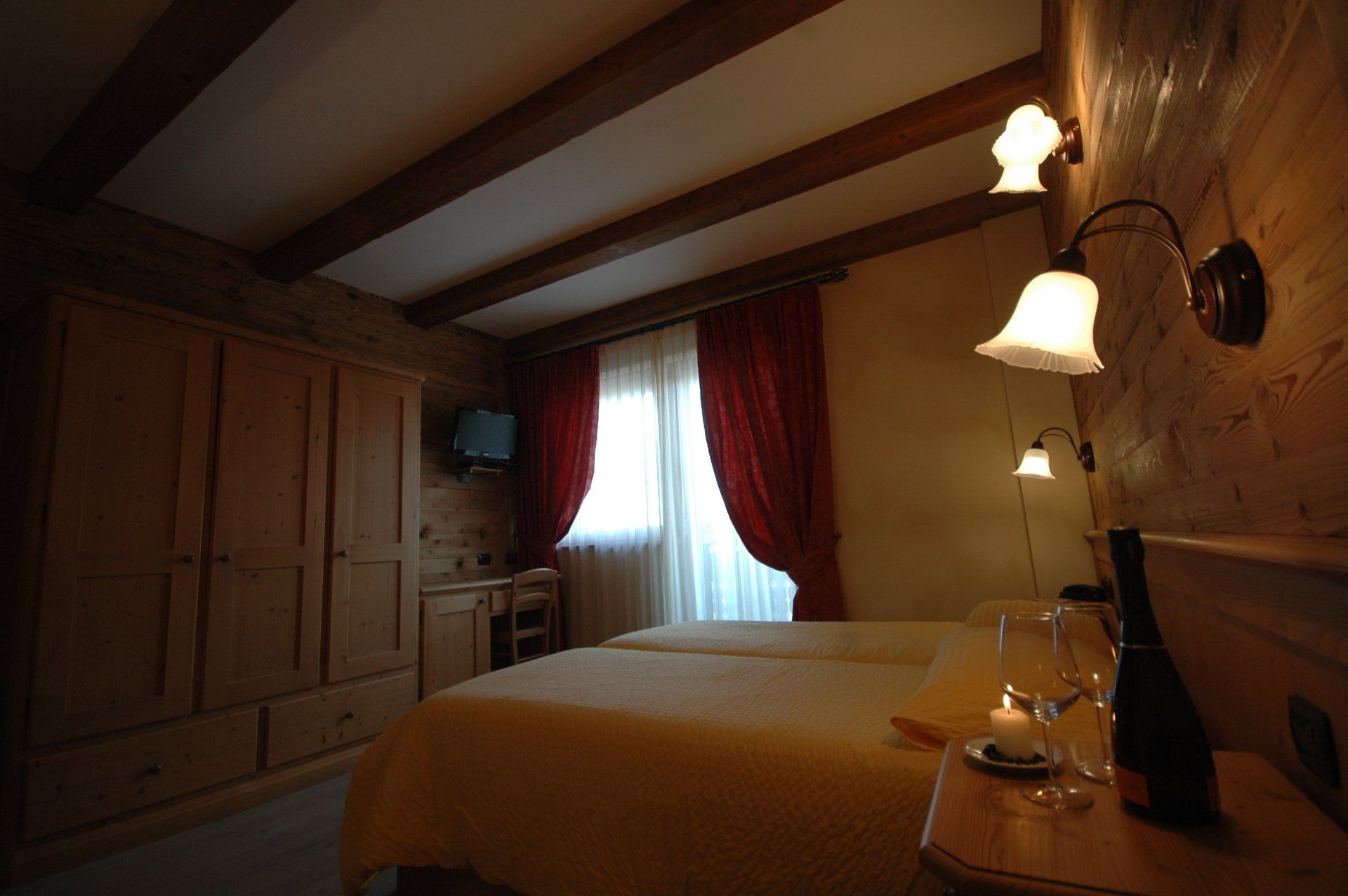 Camera da letto con letti gemelli, travi in ​​legno, armadio, tende rosse e applique.
