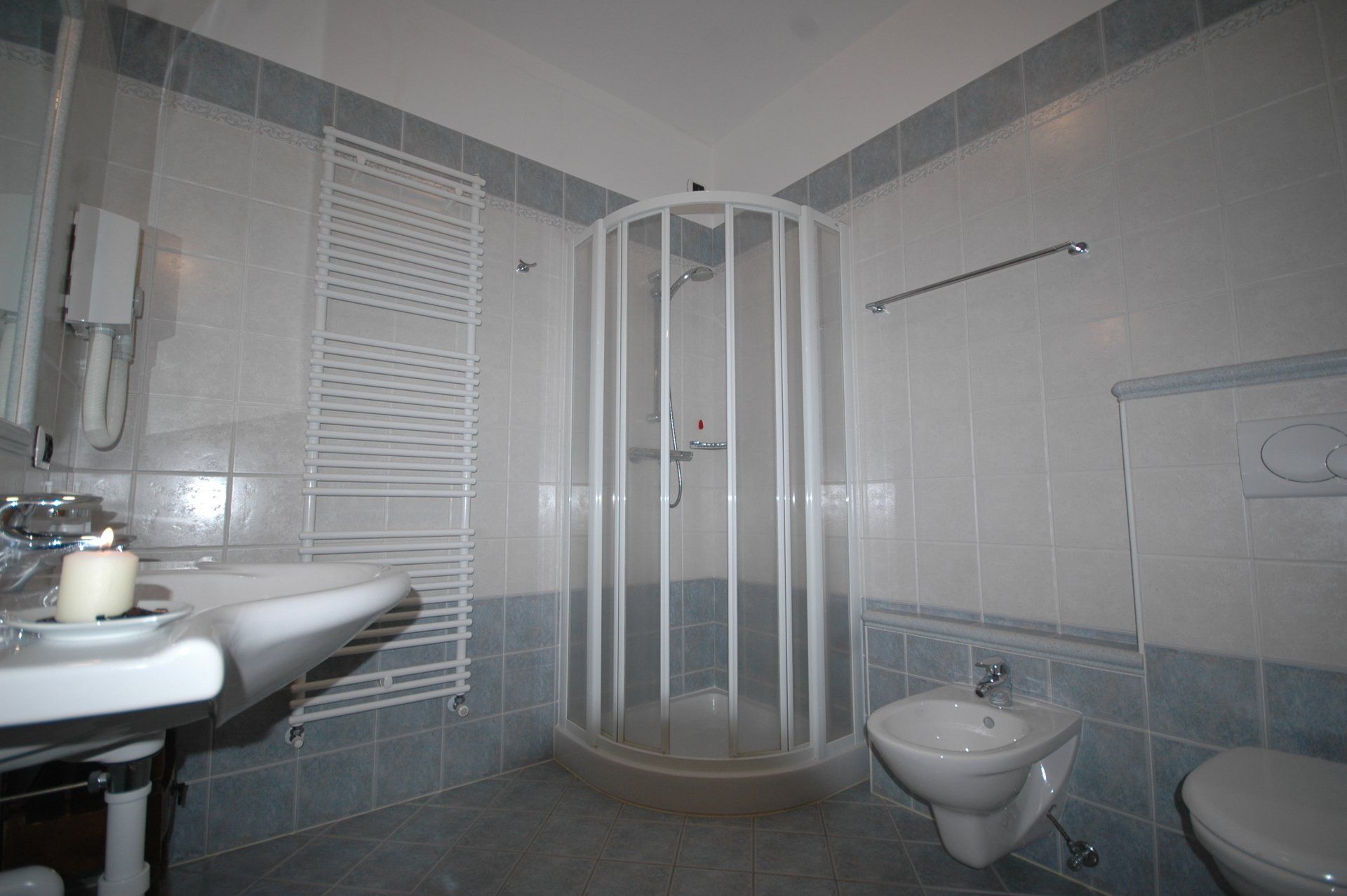 Bagno con pareti piastrellate bianche e blu, doccia, lavandino, bidet e WC.