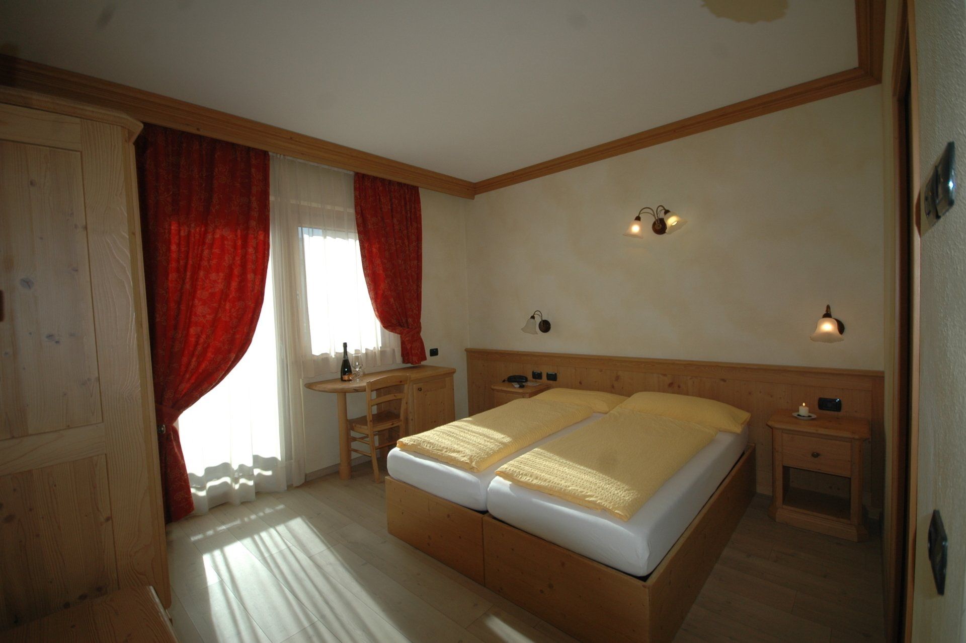 Camera da letto con letto matrimoniale, tende rosse, mobili in legno e luce solare intensa.