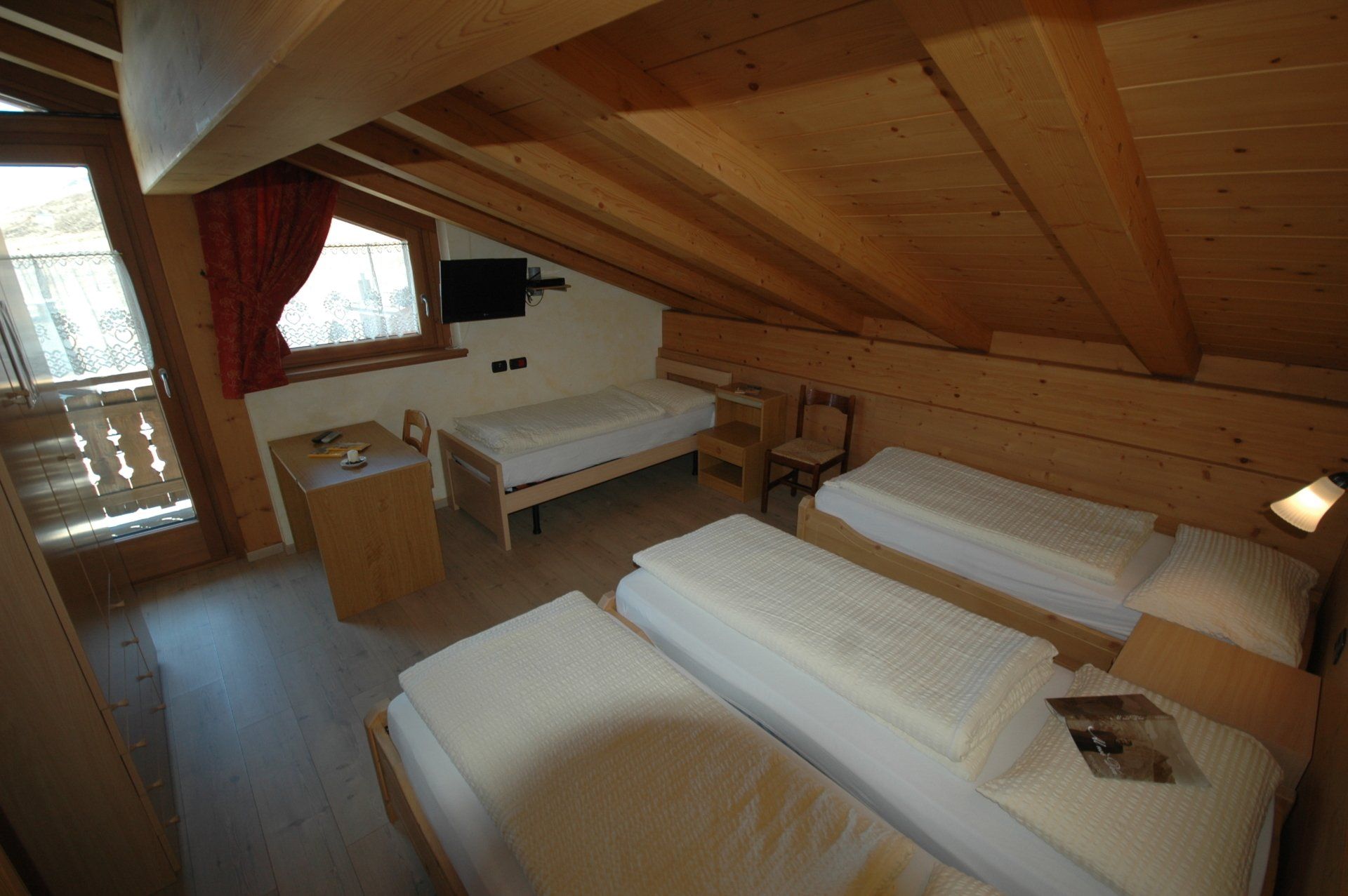 Una camera da letto mansardata con pannelli in legno, tre letti, una scrivania e una piccola TV.