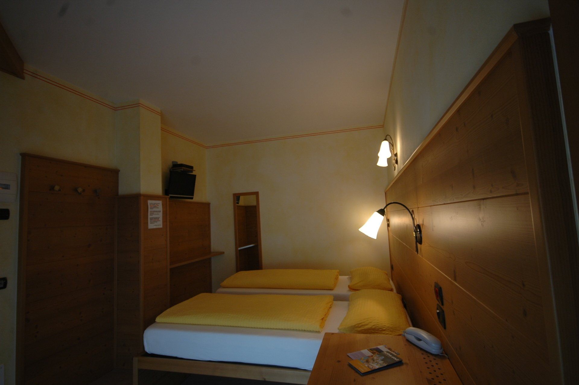 Una piccola camera d'albergo con due letti, mobili in legno chiaro e una piccola TV.
