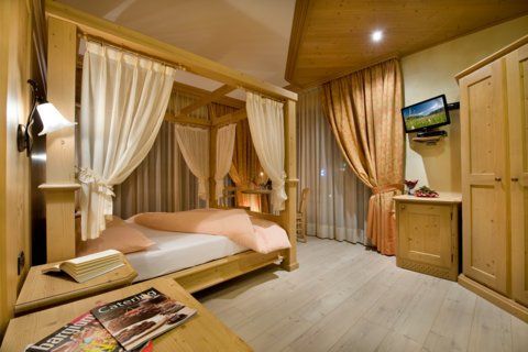 Accogliente camera da letto con letto a baldacchino, mobili in legno chiaro, TV e tende drappeggiate.