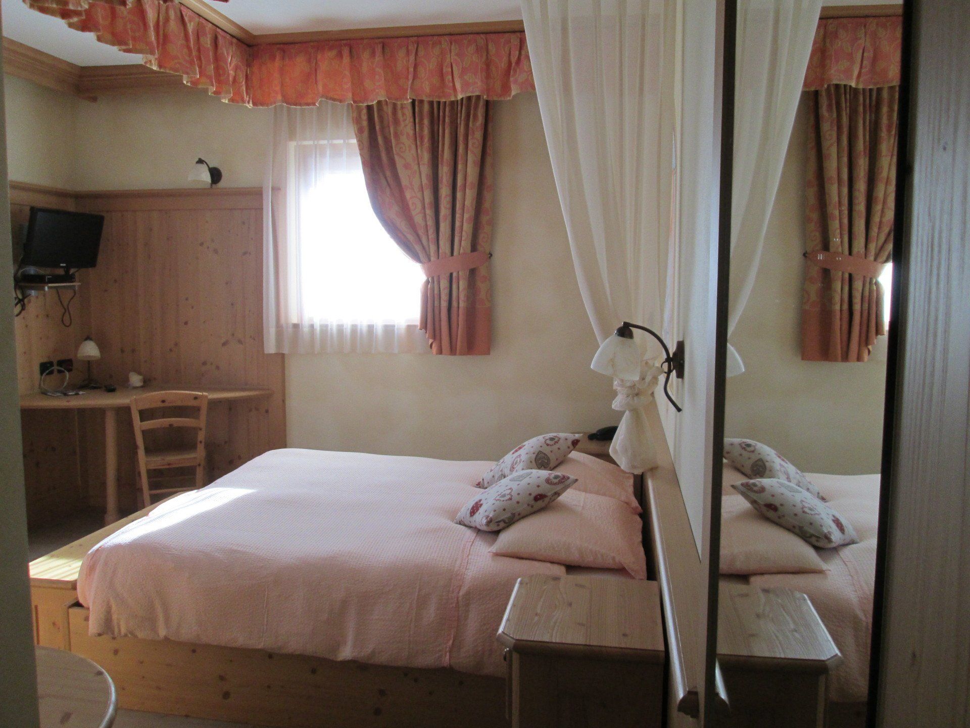 Camera da letto con letto matrimoniale, biancheria da letto rosa chiaro, mobili in legno e finestra con tende.