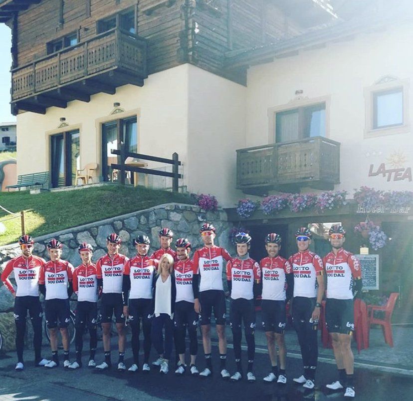 Ciclisti in divise rosse e bianche in posa davanti a un edificio, forse un bar, con la scritta 