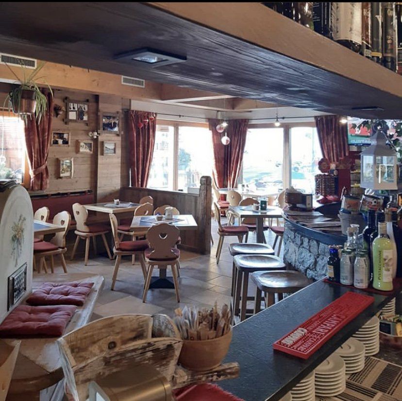 Accogliente ristorante con tavoli, sedie e bancone in legno; tende, finestre e sgabelli da bar rossi.
