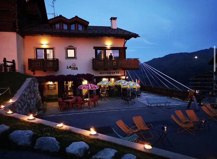 Ristorante al tramonto, in un ambiente montano con posti a sedere all'aperto, illuminato da candele e lucine.