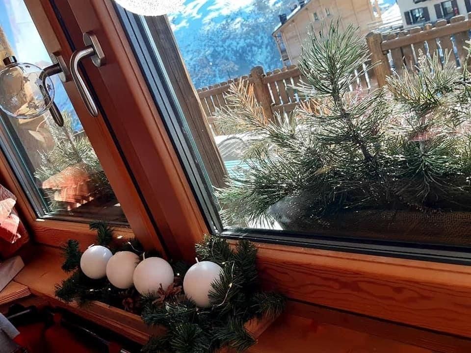 Una finestra con una ghirlanda natalizia e vista sulle montagne innevate.