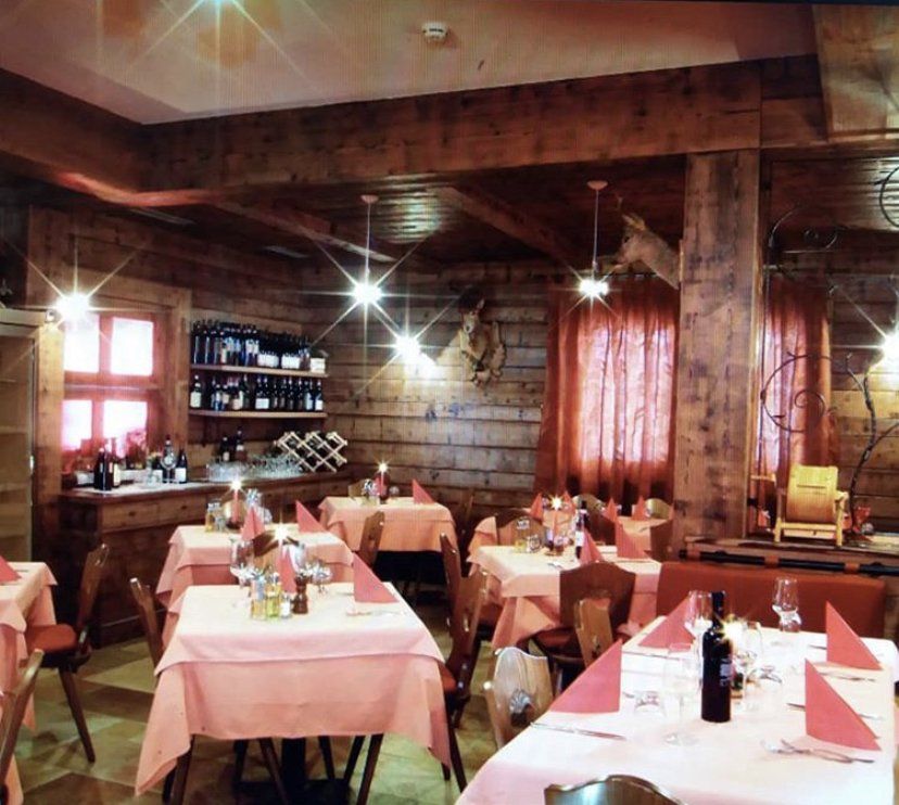 Interno del ristorante con travi in ​​legno, tovaglie rosa e bottiglie di vino.