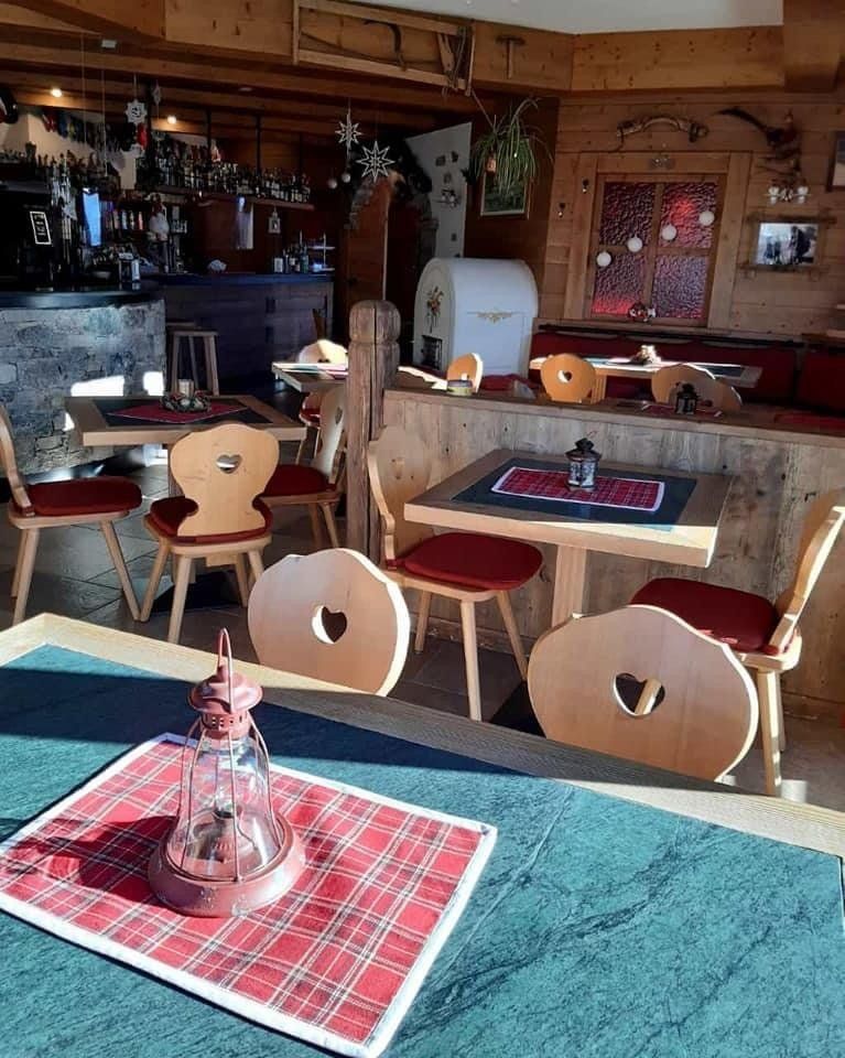 Interno di un ristorante in legno con tavoli, sedie e un bar. Cuscini rossi, luci calde.