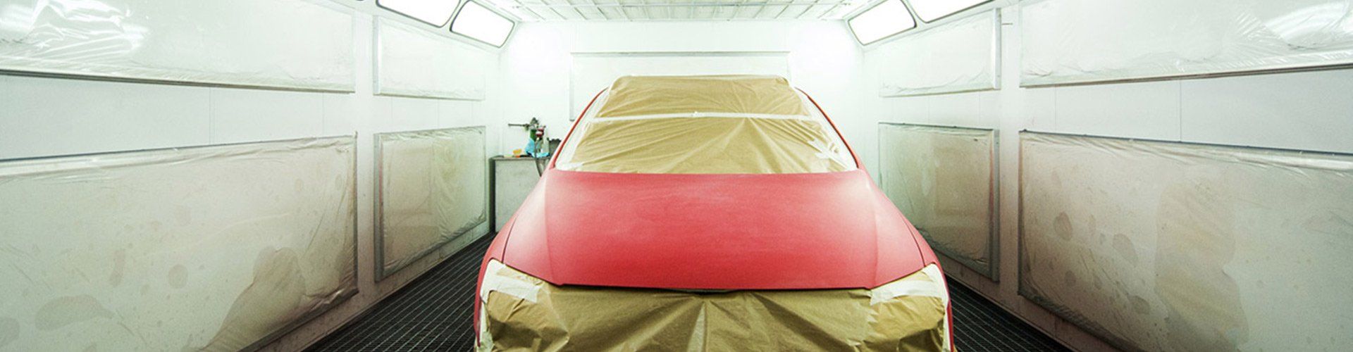 Car in a paint booth with red section taped. Beige paint booth interior.