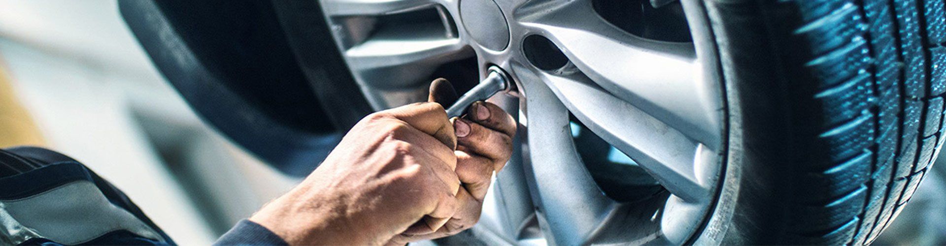 Mechanic working on a car tire, using a tool to loosen a bolt.