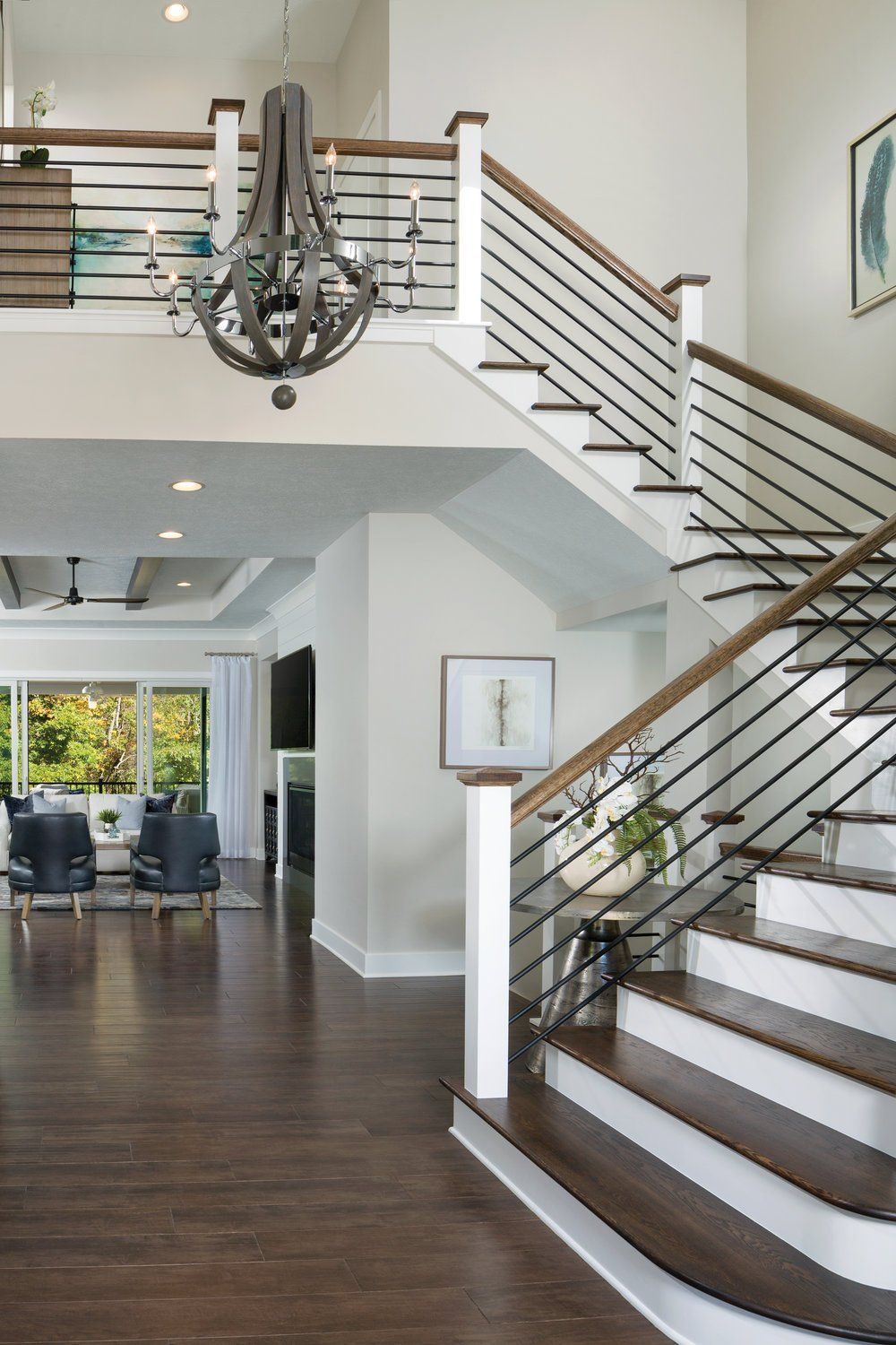An open interior view of a home with a wooden staircase, horizontal railing, a hanging chandelier, and a living area.
