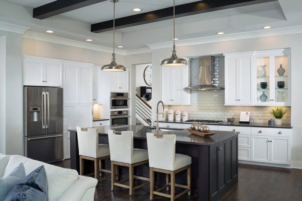 A modern kitchen with a dark central island, white cabinets, stainless steel appliances, and two hanging pendant lights.
