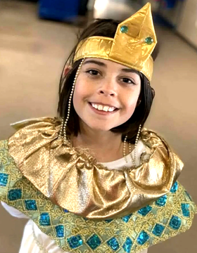 Girl in gold and teal Egyptian costume smiles, wearing a crown and collar.
