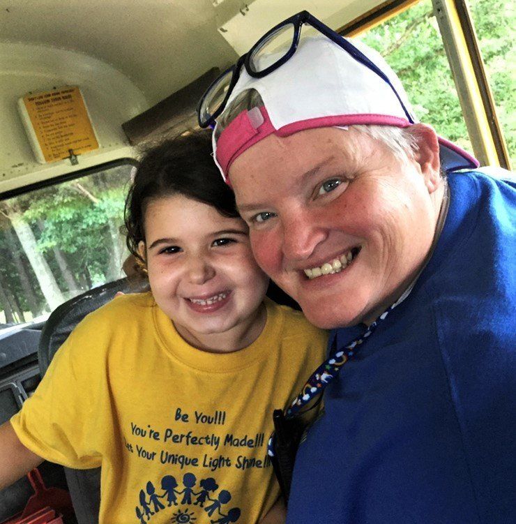 Woman and girl smiling on a bus. Woman wears a cap and glasses. Girl wears a yellow shirt.