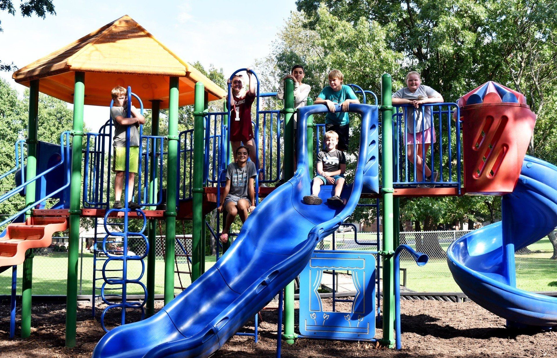 Children on a playground with a blue slide and climbing structure.