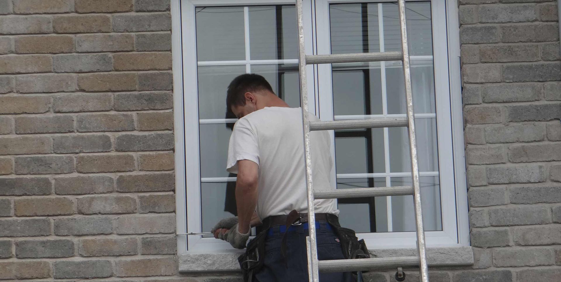 Un laveur de vitres sur une échelle, nettoyant une fenêtre sur un bâtiment en briques.