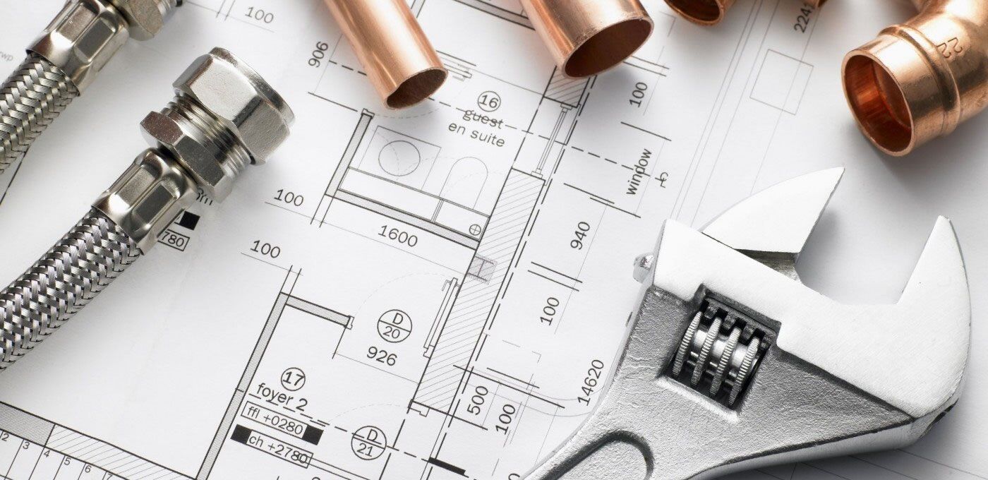 Plumbing tools including a wrench, copper pipes, and metal hoses, on a blueprint.