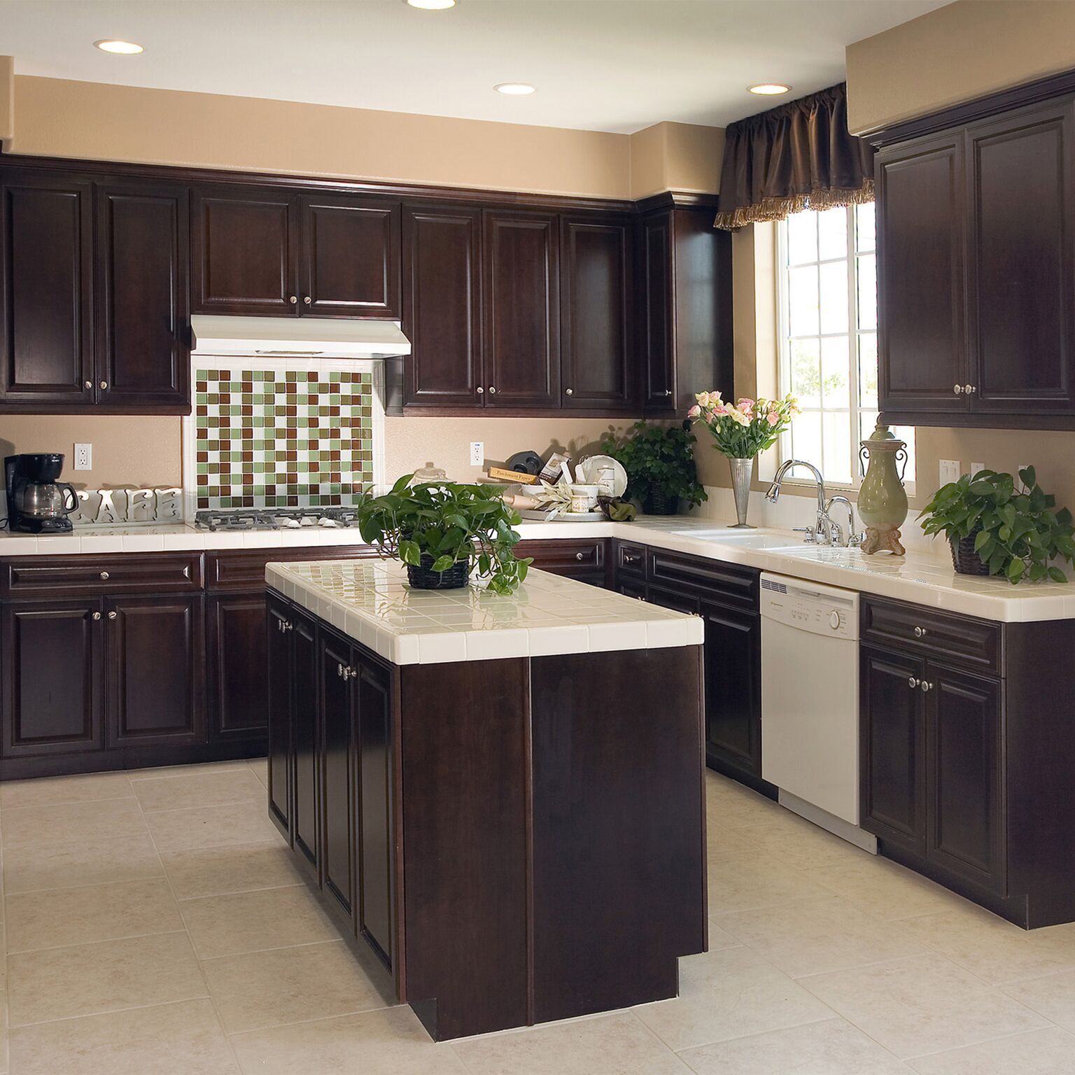 Dark wood kitchen cabinets with white countertops and an island, beige walls, and a window.