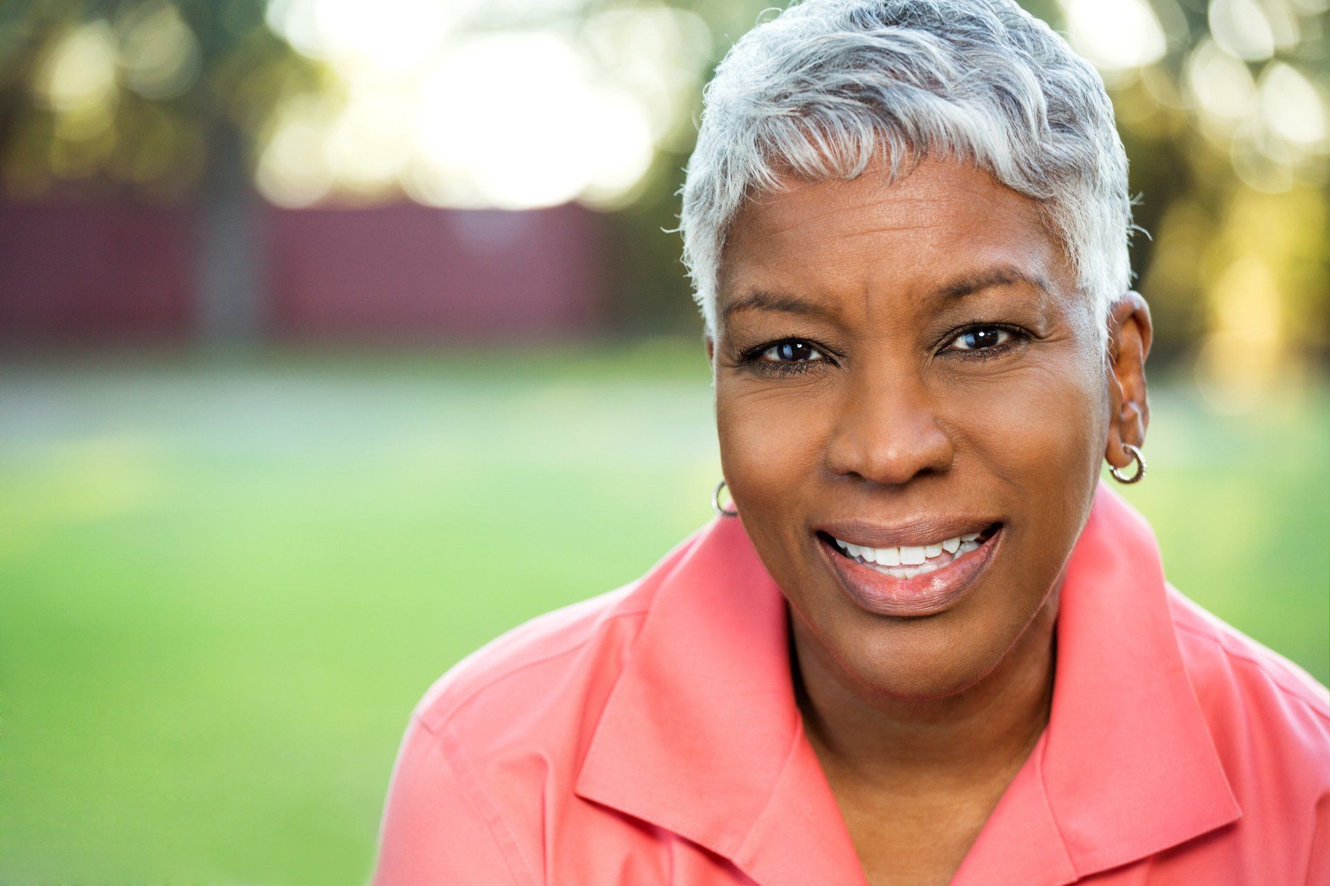 A woman with gray hair is smiling for the camera while wearing a pink shirt.