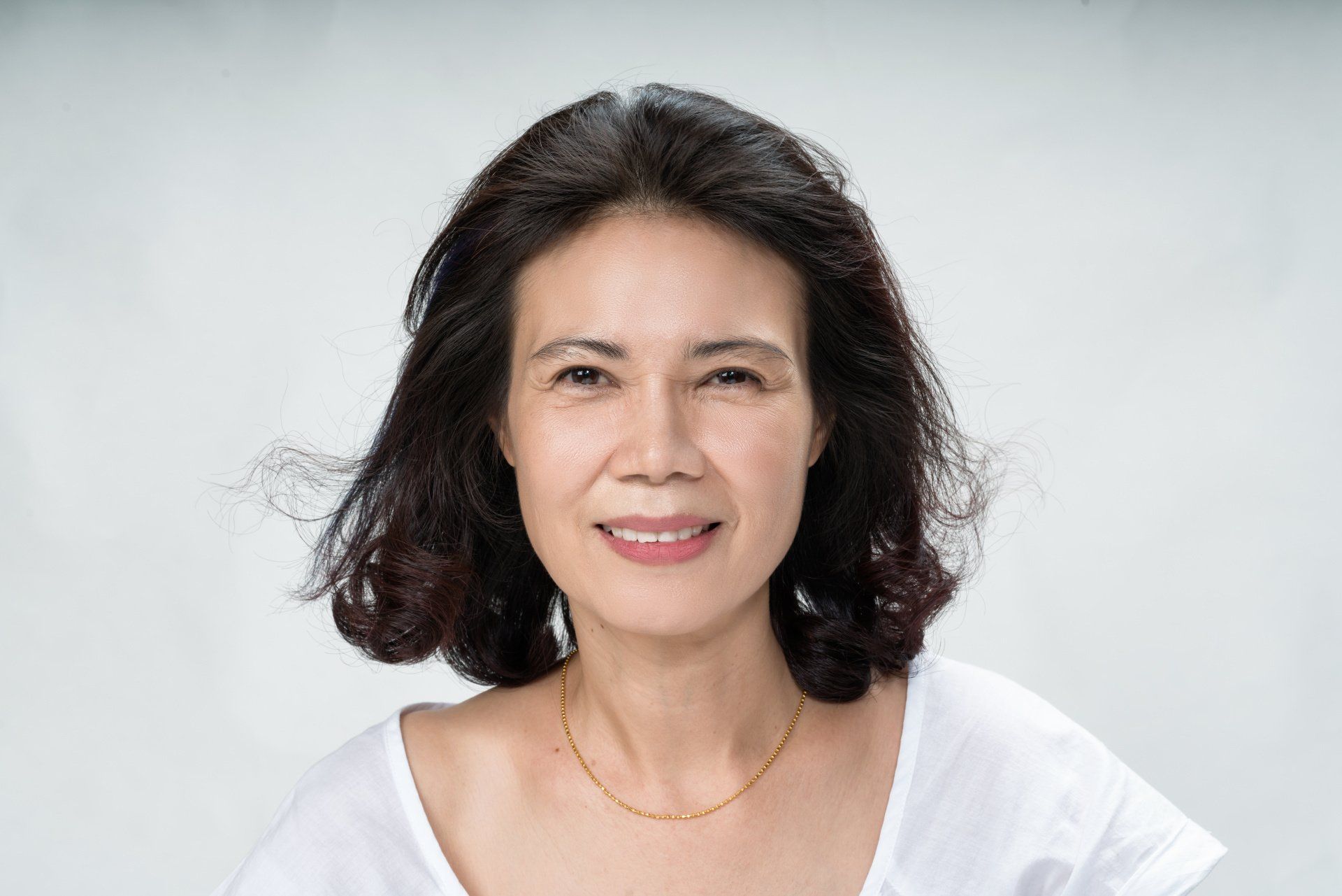 A woman in a white shirt and necklace is smiling for the camera.