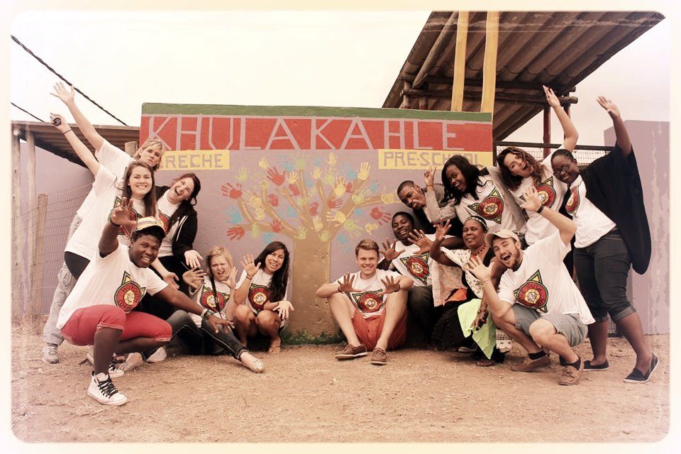 Group posing and cheering in front of a colorful “KULIAKAH?” mural under a shelter.