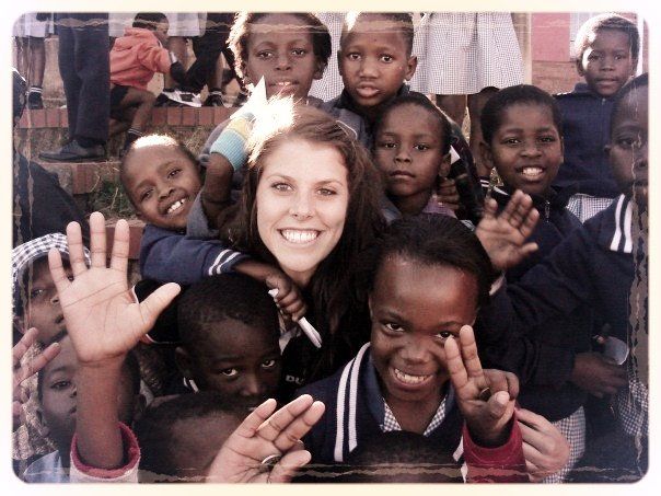 Smiling woman surrounded by children waving at the camera indoors