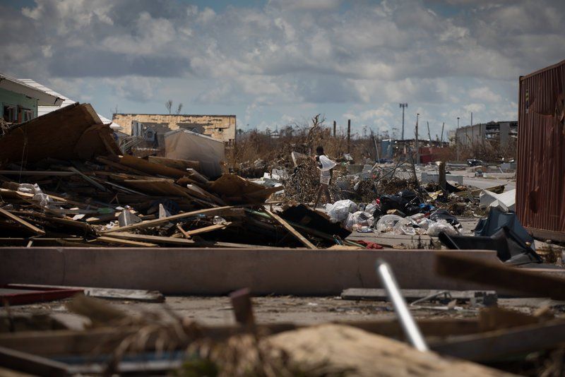 Wide view of storm debris and collapsed buildings under a cloudy sky in a devastated neighborhood
