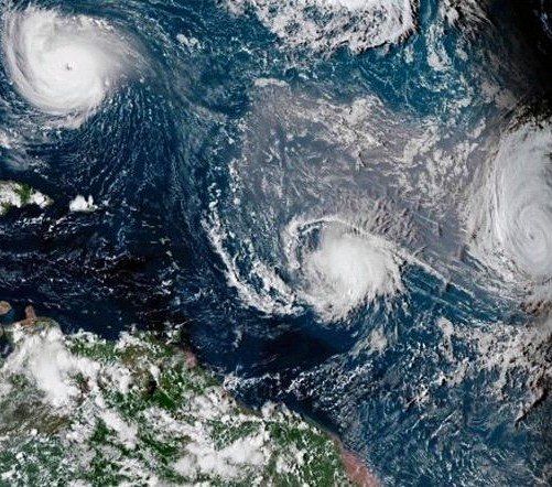 Satellite view of three swirling hurricanes over the ocean near a green coastline