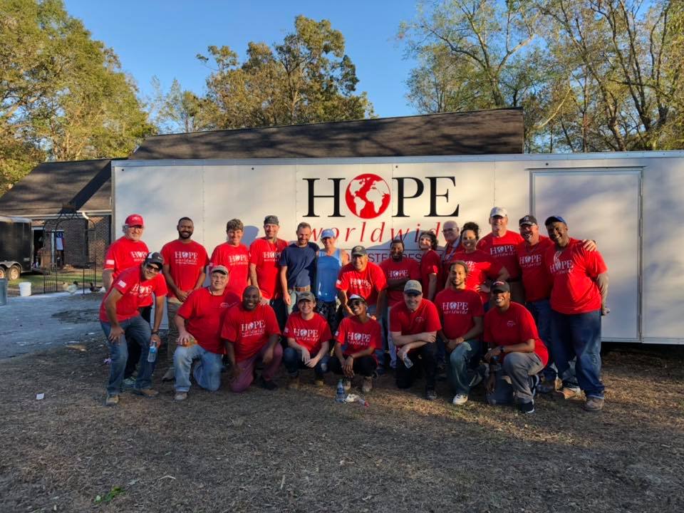 Group of volunteers in red shirts posing in front of a building labeled “HOPE Worldwide”