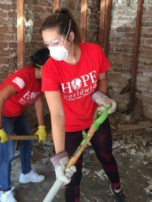 Volunteers in red shirts use shovels to clear debris inside a damaged brick building
