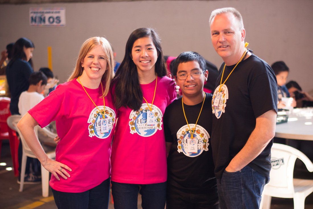 Four people in matching pink and black shirts pose together indoors, smiling at the camera.