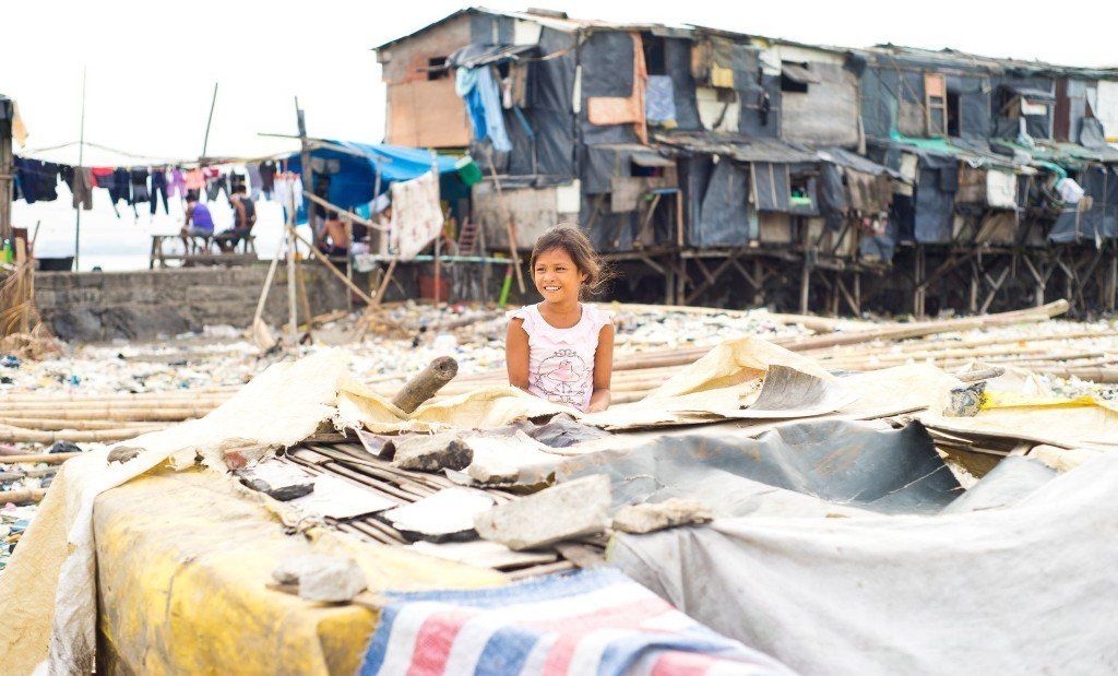Makeshift shelter in a damaged settlement with a person standing amid tarps and debris