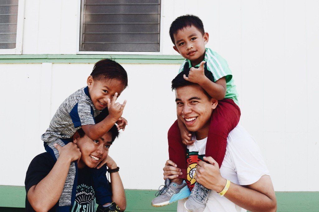 Two smiling adults carrying two children on their shoulders outside a building