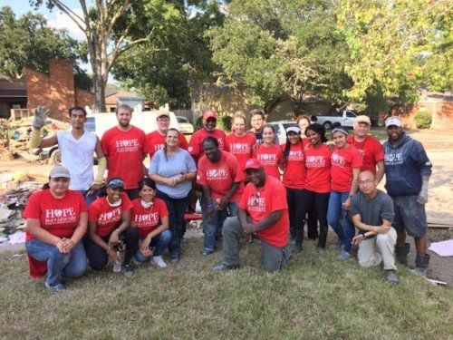 Group of people in red shirts posing outdoors on grass in front of a brick building.