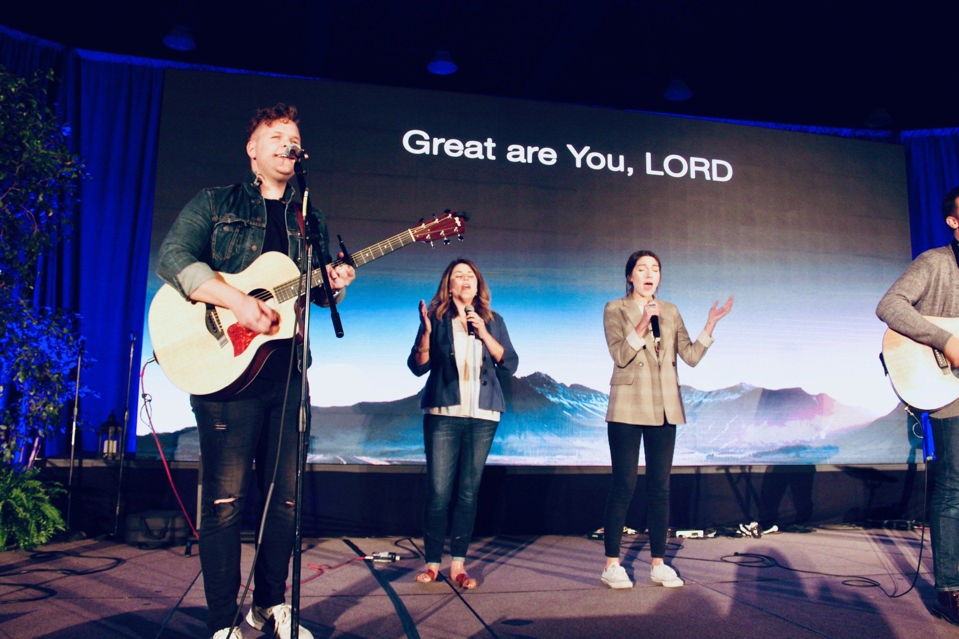 Worship band on stage under blue lights, singing and playing guitars; screen reads “Great are You, LORD”