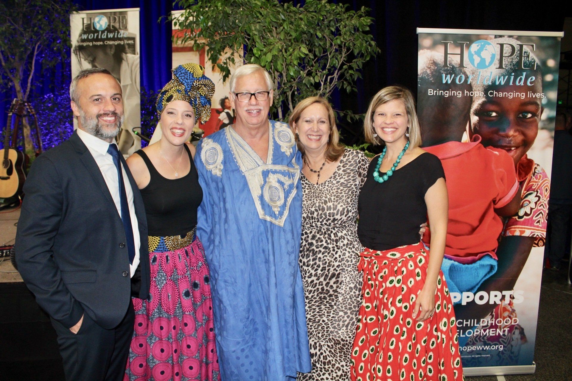 Five people posing at an indoor event with charity banners in the background.